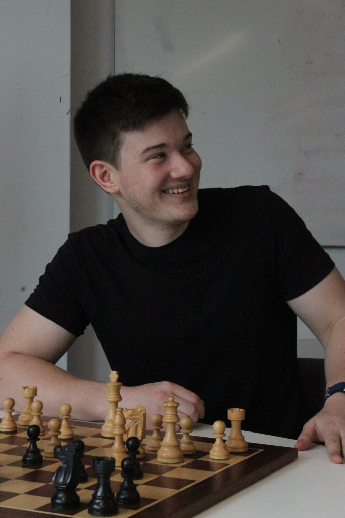 A chess player laughing and looking towards his friends during a friendly match.