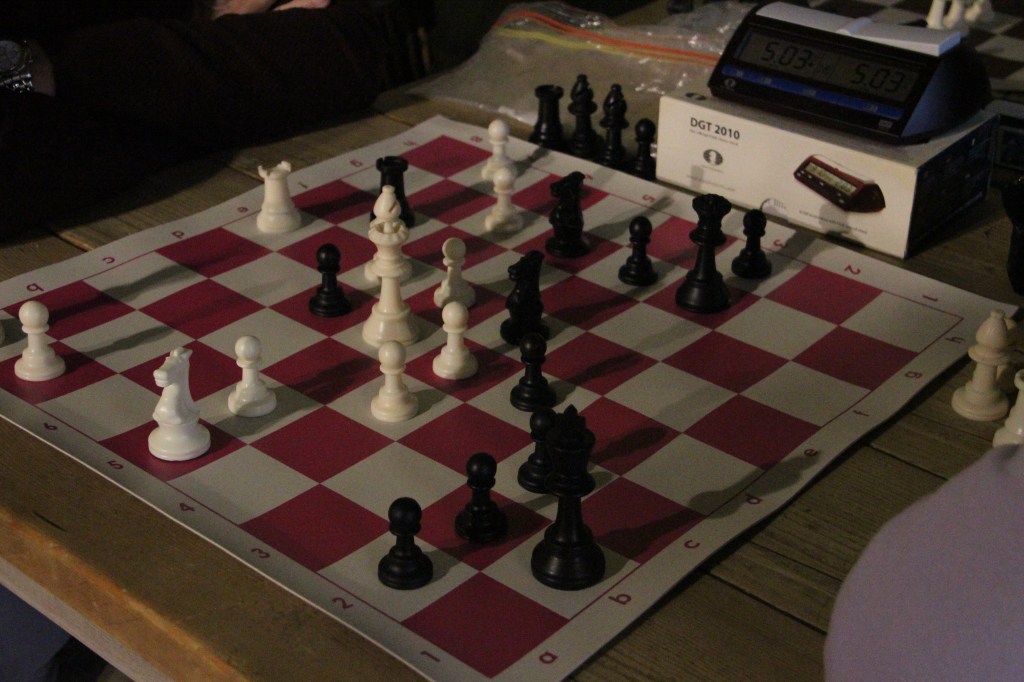A close-up of a chessboard with black and white pieces mid-game accompanied by a digital chess clock on a wooden table.