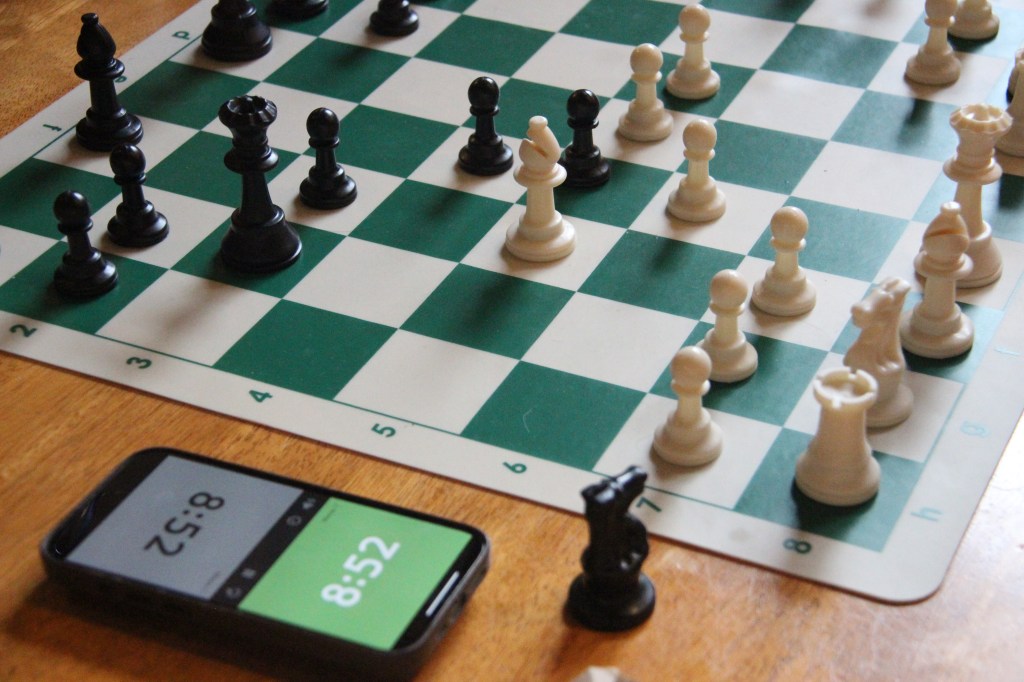 A green-and-white chessboard with white and black pieces mid-game, next to a smartphone timer showing 8:52 minutes left.