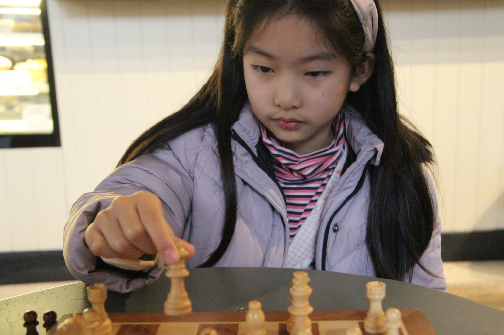 Eight-year-old girl moving a chess move at the London Chess Club.