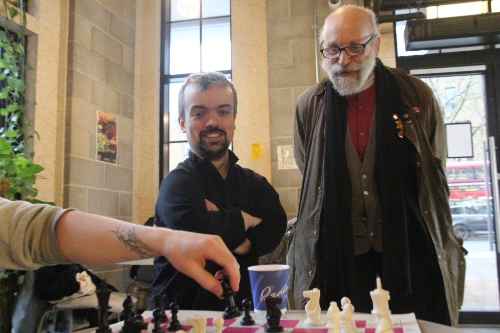 Two organisers of the London Chess Club overlooking a chess match with a person making a move.